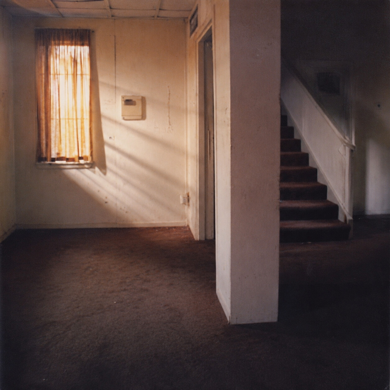 Older vacant interior with a curtained window, utility panel, dividing wall, and staircase